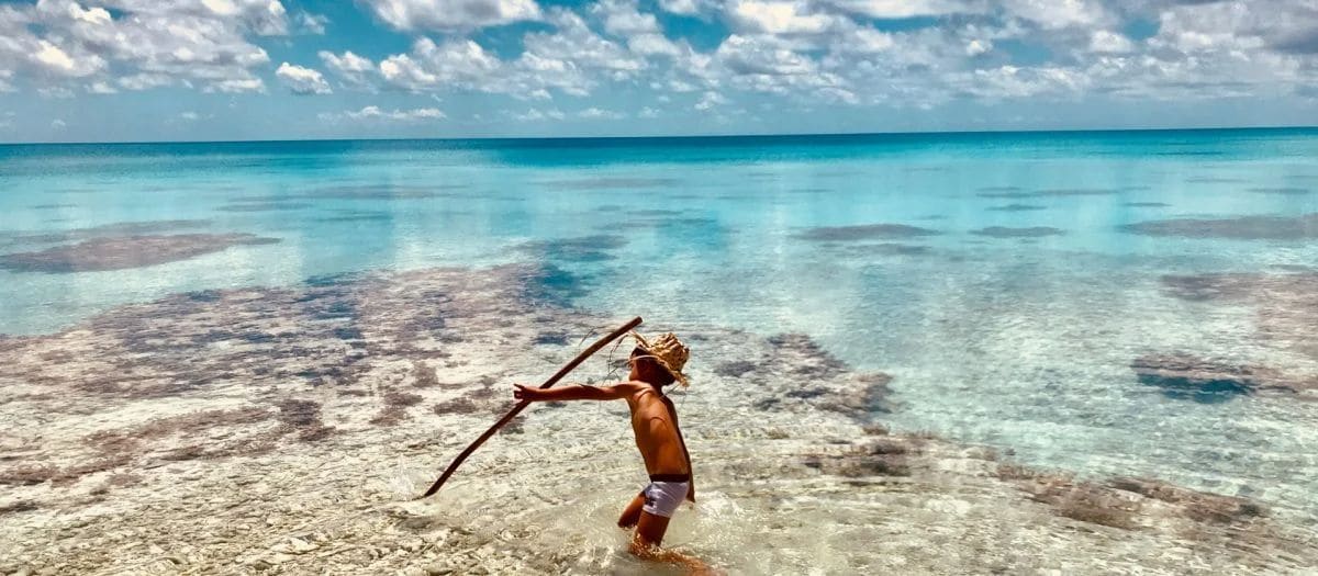 Un enfant joue avec un bâton dans le lagon, devant la pension